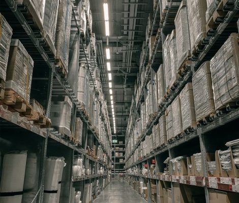 A long aisle in a modern warehouse with high shelving filled with boxes and supplies.
